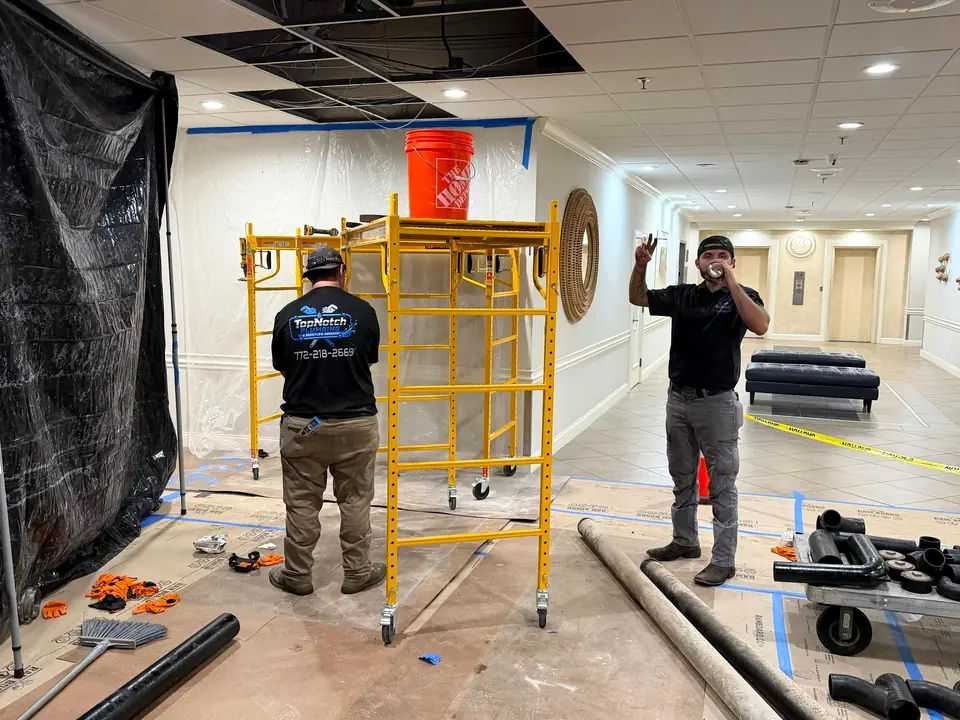 Two Top Notch plumbers working in a commercial building hallway with a rolling scaffold