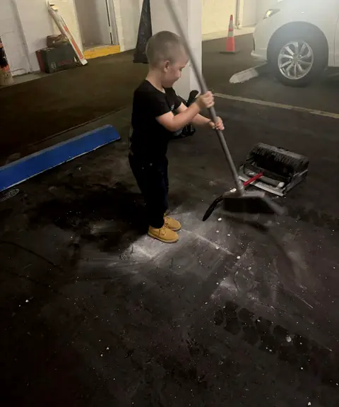 A young boy in a Top Notch shirt sweeping up on a job site