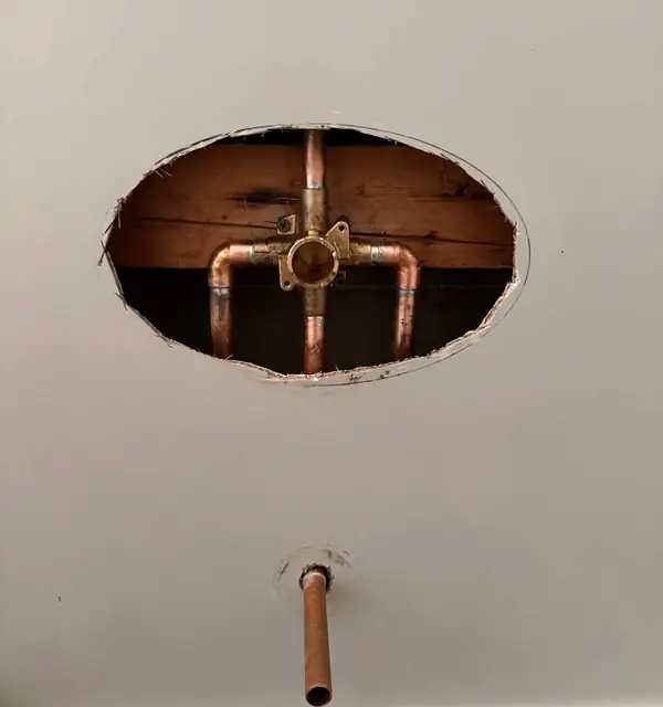 A copper shower valve roughed in through an opening in the wall