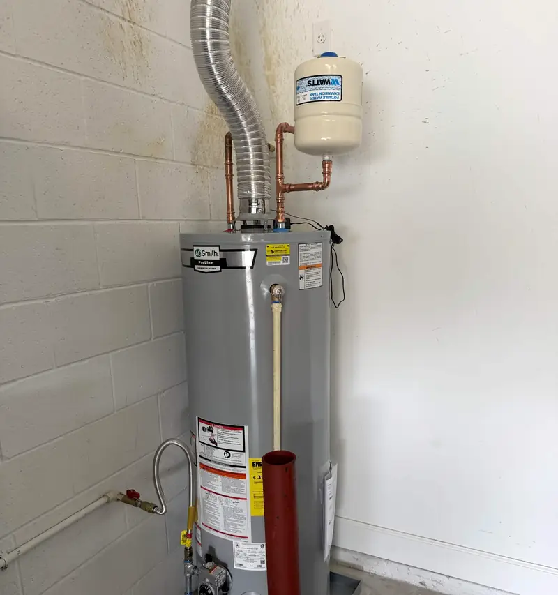 A newly installed gas water heater with copper connections and an expansion tank on the wall above it