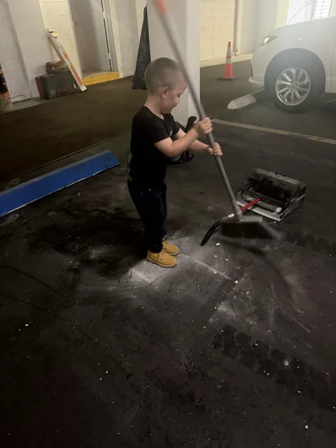 Jaxson sweeping up debris with a broom and dustpan in a parking garage