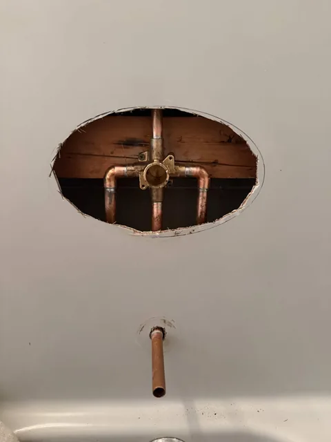 An exposed shower valve and copper pipework through an opening in the wall