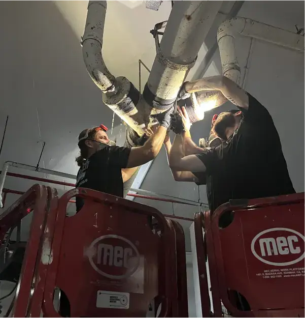 Two Top Notch techs on lifts fitting commercial overhead supply lines