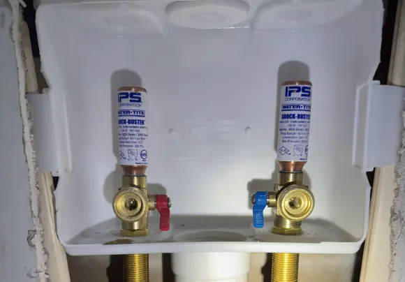 A close-up view underneath a sink showing a white plastic drainpipe connected to a chrome-plated metal p-trap assembly. The metal pipe exhibits heavy corrosion with light green and white residue. Black putty or sealant is used around the joint where the metal pipe meets the white pipe, and a gray wire is draped across the pipes.