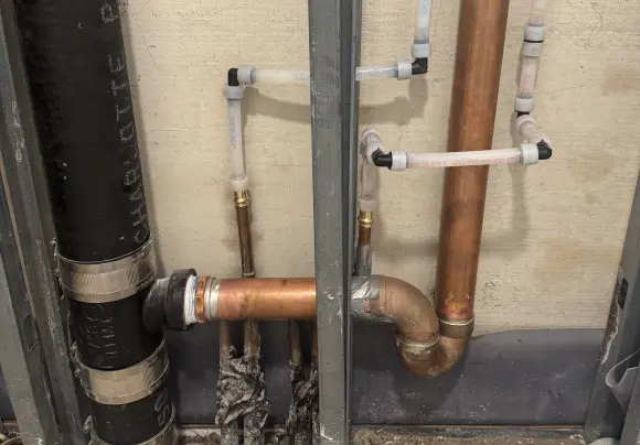 A close-up view of a partially installed brass shower or faucet valve cartridge mechanism exposed through a rectangular cut-out in drywall. The main valve body is centered, showing the brass retaining nut and a temperature limit stop or gear.